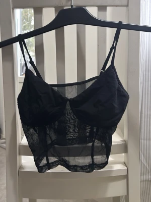 Svart mesh linnetopp med tunna band - Snygg svart linnetopp i mesh med tunna, justerbara axelband och transparent material. Toppen har en passform. Aldrig använd