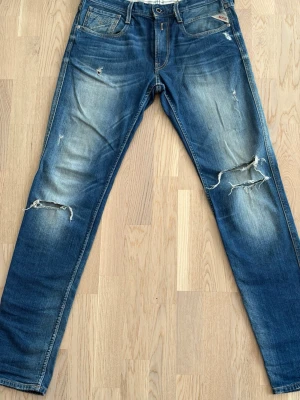 Blå slitna jeans från Replay - Snygga blå jeans från replay med slitna detaljer och hål på båda benen. Jeansen har klassisk femficksdesign, normal passform och är tillverkade i denim. Perfekta för en avslappnad och trendig look. 