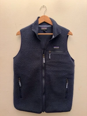 Mörkblå fleeceväst från Patagonia - Mysig mörkblå fleeceväst från Patagonia i storlek M. Perfekt till våren då den är lite varmare och otroligt snygg. Skick 9/10, använd några få gånger. Skriv om ni har några fler frågor!