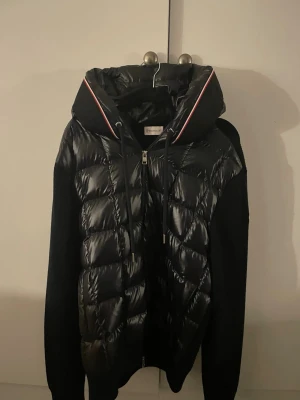 Svart/marinblå Moncler cardigan med huva - Säljer en svart/marinblå cardigan från Moncler. Jackan har hel dragkedja, ribbade ärmar och diskret Moncler-logga på ärmen. Materialmix med blank polyester framtill och stickade ärmar och rygg. Knappt använd, orginalbox finns med och skickas i den, nypris 12300, hör gärna av dig vid eventuella frågor!