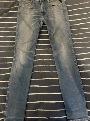 Ljusblå replay anbass  - Snygga ljusblå slim fit jeans(replay anbass)med slitningar och tvättade detaljer från. Klassisk femficksmodell med normalhög midja och raka ben. Jeansen har kontrastsömmar och patch bak i midjan. Perfekta till en avslappnad streetstil. Köpta för 750 här på Plick, kan gå ner i pris vid snabb affär!