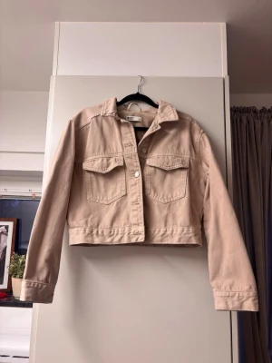 Gina tricot Perfect Jeans beige jacka, storlek S - Snygg beige croppad jeansjacka från Gina tricot med klassisk krage och två stora bröstfickor. Jackan har långa ärmar och stängs med knappar framtill. Perfekt att slänga över en hoodie eller t-shirt för en chill look.