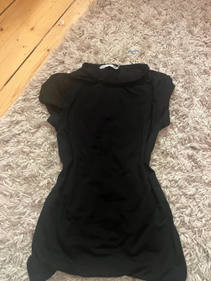 Svart kortärmad tröja - En enkel och stilren svart tröja med korta ärmar och hög hals. Tröjan har en kroppsnära passform och är perfekt för dig som gillar minimalistisk stil. Materialet känns mjukt och stretchigt, vilket gör den bekväm att bära. Tröjan är i trängnings material och är jätte bekväm!