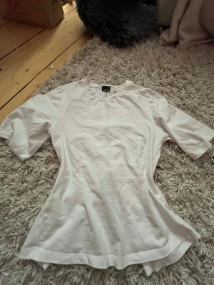 Vit topp med knyt i ryggen - Säljer en vit topp med korta ärmar och snygga knytband i ryggen. Modellen är figurnära och har en enkel, stilren look som passar till det mesta. Tillverkad i mjuk bomull för en skön känsla hela dagen.