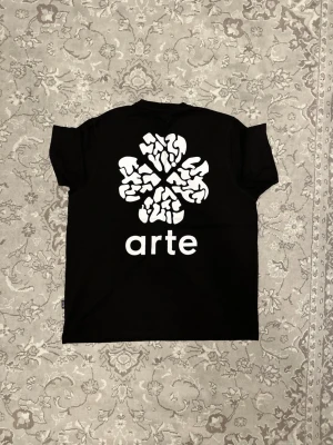 Svart t-shirt från Arte med tryck - Svart t-shirt från Arte med stort vitt grafiskt tryck och texten 'arte' på ryggen. Klassisk passform och rund hals. Perfekt för dig som gillar streetwear och vill sticka ut med en unik design.
