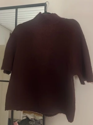 Mörkbrun stickad tröja med halvärm - Mysig vinröd stickad tröja med halvärm och hög hals. Tröjan har en avslappnad passform och är perfekt för lager på lager. Passar dig som gillar en enkel men stilren look.