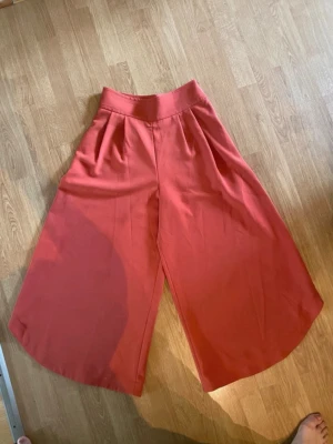 Korallfärgade wide byxor See By Chloé - Snygga korallfärgade byxor från See By Chloé i modell wide med hög midja. Byxorna har ett luftigt och croppat snitt, tillverkade i mjukt tyg som ger en skön känsla. Perfekta för dig som gillar statement-plagg och vill sticka ut med färg.