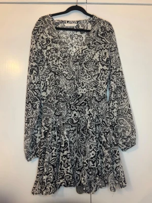Svartvit kortklänning - Kort klänning i svartvitt med v-ringning och långa ärmar. Jätte fin klänning för sommar och vardags! Endast använd 1 gång!