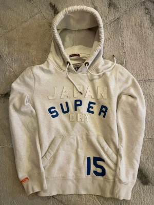 Grå superdry hoodie - En oversized grå tjock hoodie i storlek M. Vit och blå text. Jätte fin och skön. Säljer då den inte passar mig. Den är väldigt eftertraktad & sällsynt i äkta vintage/y2k stil ✨. Svår att få tag på idag. Storlek M passar lite större. Skickas inom 24h. 💬 går att diskutera vid snabb affär.