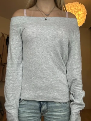Ljusgrå offshoulder långärmad topp - Ljusgrå långärmad topp med offshoulder-design. Mjuk och stretchig i materialet, perfekt för en avslappnad och trendig look. Slitasde ärmar. 