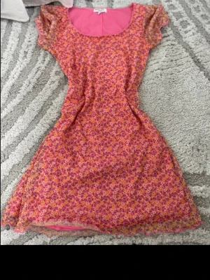 Blommig kortklänning Brave Soul - Söt kortklänning från Brave Soul i rosa med små blommor i lila och gult. Klänningen har rund halsringning, korta ärmar och figurnära passform. Perfekt för varma dagar och ger en färgglad vibe.