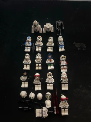 LEGO Star Wars minifigurer samling - Samling med LEGO Star Wars minifigurer, främst klontrupper och stormtroopers i olika varianter och färger. Inkluderar hjälmar, vapen och tillbehör samt en droid och en figur med blå mantel. Perfekt för dig som gillar Star Wars och LEGO.