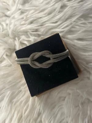 Silvrigt armband med knutdetalj - Snyggt armband i silverfärgad metall med en unik knutdetalj framtill. Armbandet har en mesh-liknande struktur och stängs med ett magnetlås. Perfekt accessoar för att lyfta din outfit med en cool och modern touch.