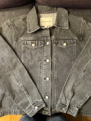 Grå jeansjacka från Carin Wester - Snygg grå jeansjacka från Carin Wester med klassisk krage, bröstfickor med lock och silverfärgade knappar framtill. Jackan har en rak passform och långa ärmar, perfekt för en cool och avslappnad stil.