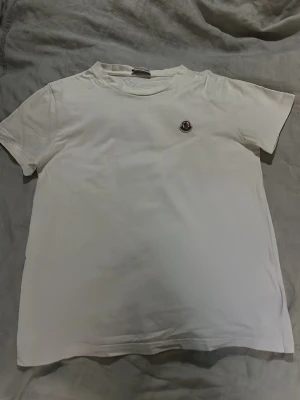 Moncler T-Shirt - Hej! Jag säljer en riktigt stilren vit moncler T-Shirt! Den är i övrigt bra skick förutom att det finns några hål i armhålorna men inget som man riktigt ser när man har på sig den, den är gjord i ett mycket mjukt bomulls material så den är riktigt bekväm. Storlek 14y vilket motsvarar typ S man. Självklart äkta✅