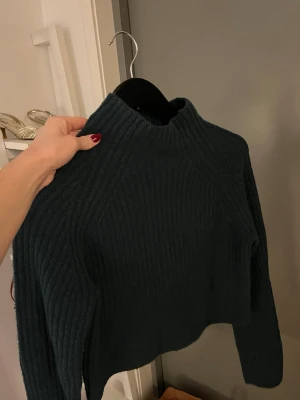 Mörkgrön stickad tröja - Säljer en mörkgrön ribbstickad tröja med hög hals. Materialet är väldigt mjukt. Storlek xs från monki. 