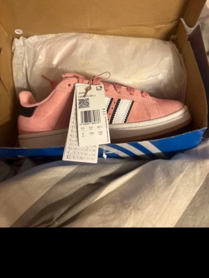 Adidas Campus rosa sneakers - Säljer ett par Adidas Campus sneakers i en snygg rosa färg med vita och svarta detaljer. Skorna har klassiska snörningar, platt sula och är tillverkade i mocka för en soft vibe. Perfekta för dig som vill sticka ut med stilrena och trendiga sneakers. Aldrig använt 