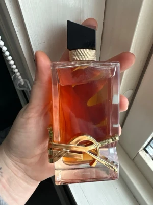 Yves Saint Laurent Libre EdP - Säljer en ikonisk Yves Saint Laurent Libre Eau de Parfum. Flaskan är rektangulär i tjockt glas med en elegant guldig YSL-logga runt botten och svart asymmetrisk kork. Innehållet är bärnstensfärgat och flaskan har exklusiv känsla.