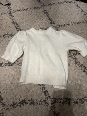 Vit stickad tröja med puffärm - Snygg vit stickad tröja med puffärmar och rund halsringning. Tröjan har ribbstickade muddar vid ärmslut och nederkant, vilket ger en stilren look. Perfekt för dig som gillar en enkel men trendig stil.