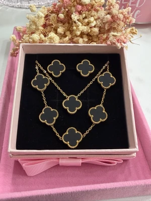 Klöver-set - Elegant och stilrent klöver-set i vacker svart färg som ger en lyxig och trendig känsla. Setet består av halsband, armband och örhängen, tillverkat i högkvalitativt rostfritt stål med exklusiv 18K guldplätering. Klöverdesignen i 15 mm ger ett tidlöst och feminint uttryck som passar både vardag och fest. Armbandet har en längd på 17,5 cm till första ringen samt 5 cm förlängningskedja för optimal och justerbar passform. Setet levereras i en elegant ask, perfekt som present.