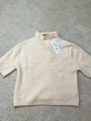 Beige stickad topp med polokrage - Säljer en beige stickad topp med polokrage och korta ärmar. Enkel och stilren design som passar perfekt till många outfits. Mjuk och skön kvalitet, perfekt för dig som gillar minimalistisk stil.