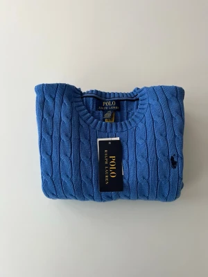 Blå kabelstickad tröja Polo Ralph Lauren - Blå kabelstickad tröja från Polo Ralph Lauren i storlek 14-16 vilket ungefär motsvarar XS. Klassisk och tidlös modell med broderad Polo-logga på bröstet. Tröjan är köpt i USA och går därför inte att lämna tillbaka. Den är i mycket fint skick, helt oanvänd med prislapp kvar. Ett stilrent plagg av hög kvalitet som passar perfekt nu till lite kyligare väder, både till vardags och mer uppklädda tillfällen. Vid frågor eller funderingar hjälper jag gärna till Mvh Olof.
