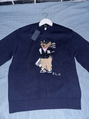 Ralph Lauren stickad tröja Polo Bear - Väldigt bekväm mörkblå stickad tröja från Polo Ralph Lauren med ikoniska Polo Bear-motivet framtill. Björnen har golfkläder och klubbor, och RLX-broderi finns nedtill. Perfekt nu i vintern och inför våren. Storlek L men passar M väldigt bra. Pris går att diskutera enbart vid snabbaffär.