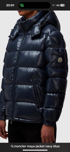 Moncler Maya pufferjacka marinblå - Säljer en Moncler Maya pufferjacka i marinblått med glansig finish. Jackan har huva, dragkedja framtill och Moncler-logga på ärmen. Den är vadderad och har en modern, chunky look som är perfekt för kalla dagar. Tyvärr har jackan ett litet hål i luvan men det är ett enkelt fix kan tänka mig gå ner lite snabb affär 
