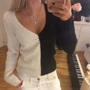 Svartvit ribbad stickad tröja - Säljer en snygg ribbstickad tröja i svart och vitt med v-ringad hals. Tröjan har lång ärm och är delad mitt på i två färger, vilket ger en cool kontrast. Perfekt för dig som gillar unika plagg med lite edge.