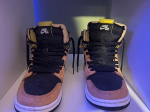 Air Jordan 1 High Zoom Air CMFT Black Monarch - Nike Air Jordan 1 Zoom sneakers i high modell med svart och orange mocka och textil. Skorna har vit swoosh, svart snörning och Zoom Air-logga på plösen. Insidan är gul och sulan är vit med svart yttersula. Perfekt för dig som gillar streetwear och vill sticka ut. Är lite smutsiga på bilden men typ aldrig använda och kommer rengöras innan de skickas.