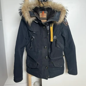 Parajumpers svart parkajacka med päls - Svart Parajumpers jacka med väldigt fin päls Modell Doris. Saknar andra knappen uppifrån, dragkedjan fungerar som den ska men har släppt lite i sömmen nedtill. Lite sminkrester som jag bifogat bild på kragen. Går allra säkrast att få bort! 