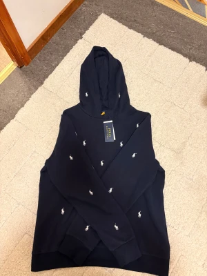 En mörkblå Polo Raulph Lauren hoodie  - En otrolig fin hoodie som är ny med prislapp och som är i underbar skick. Finns inget fel med den och rekommenderas verkligen! Storleken är 170 cm(15 år).