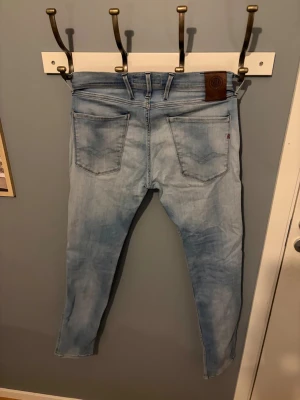 Replay Anbass ljusblå jeans slim fit - Säljer ett par Replay Anbass jeans i ljusblå tvätt med klassisk femficksdesign och inga defekter. Jeansen har slim fit passform, normal midja och är tillverkade i mjukt stretchigt denim för extra komfort. Perfekta för dig som gillar en modern och stilren look.
