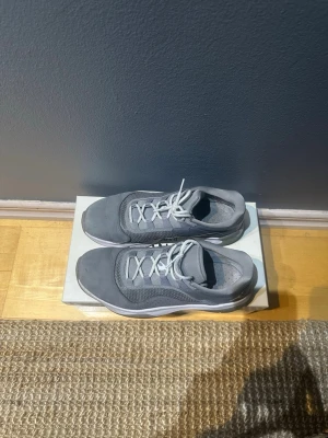 Grå Nike sneakers storlek 41 - Säljer ett par grå Nike sneakers i storlek 41. Skorna har en sportig design med mesh och syntetmaterial, vita snören och en platt sula. Perfekta för dig som gillar en clean och stilren look till vardags. Modellnummer CW0784-007.