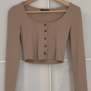 Trendig beige croppad topp i XS från SHEIN - • Trendig beige croppad topp i XS från SHEIN med långa ärmar och snygga knappar framtill. • Toppen är ribbad och har en rundad halsringning. • Oanvänd.  #croppadtop  #shein  #trendig  #långärmadtopp  #croppedtop  #topmedknapper  #