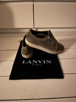 Lanvin grå sneakers med mocka och skinn - Snygga sneakers från Lanvin i grå mocka med beige skinn på tån och häl. Klassisk rund tå och platt sula, med snörning framtill. Kommer med original dustbag. Perfekt för dig som gillar stilrena och lyxiga sneakers med exklusiv känsla.