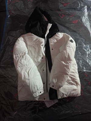 Vit pufferjacka från Moncler med huva - Säljer en snygg vit pufferjacka från Moncler med svart huva. NFC chip finns i armen vid loggan. Perfekt kvalité 