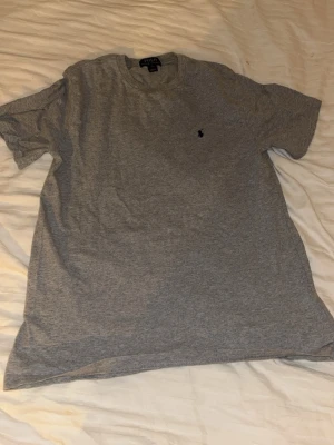 Grå t-shirt från Polo Ralph Lauren XS - Snygg grå t-shirt från Polo Ralph Lauren i storlek L. Klassisk rund hals och korta ärmar, med den ikoniska lilla broderade loggan på bröstet. Tillverkad i mjuk bomull som är skön mot huden. Perfekt för en chill och stilren look.