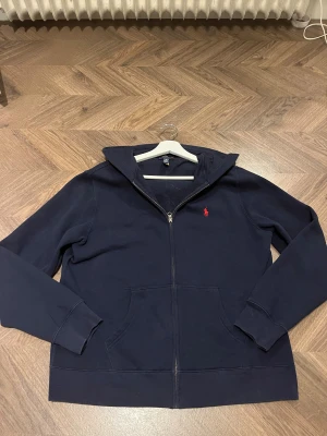 Marinblå hoodie från Polo Ralph Lauren - Säljer en fet hoodie från ralp lauren!! Är i mycket bra skick, snarare säga ny(använd 2 gånger) Den sitter som en smeck och har ett schysst material. Priset är inte hugget i sten och kan diskuteras vi intresse. Tveka inte!! 🤩🙌
