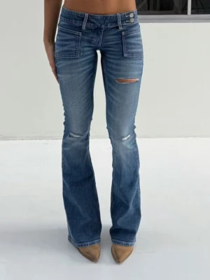 Blå bootcut jeans från Gina Tricot - Snygga blå bootcut jeans från Gina Tricot med låg midja och slitna detaljer på benen. Sne knäppning framtill💕💕 Skriv för egna bilder! Använda enbart 1 gång