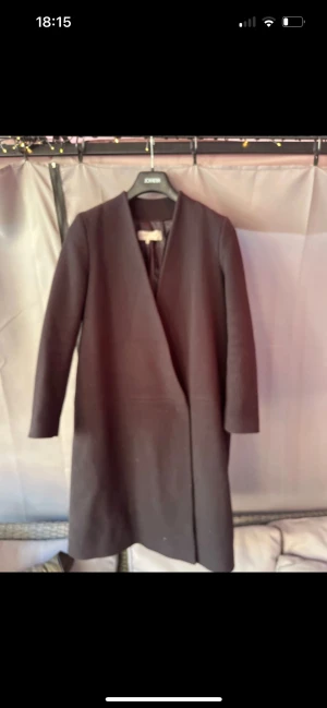 Mörk blå kappa från Gerard Darel - Stilren mörk blå kappa från Gerard Darel i klassisk omlottmodell utan krage. Långärmad och med rak passform, tillverkad i en mix av ny ull, polyamid, polyester och viskos. Perfekt för dig som gillar minimalistisk och clean look.