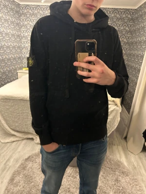 Svart Stone Island hoodie med huva - Svart hoodie från Stone Island i storlek M med klassisk patch på vänster ärm. Perfekt för dig som gillar sköna hoodies med clean stil. Den är helt ny. Säljer denna pga att den var för liten på mig. Passformen är bra i ärmarna men något kort på kroppen