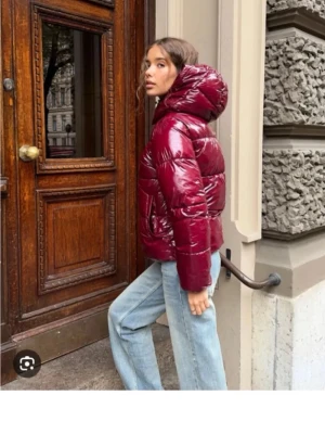 Vinröd glansig pufferjacka med huva - Säljer en vinröd pufferjacka med glansig finish och stor huva. Jackan har dragkedja framtill, två fickor och en riktigt puffig look. Köptes förra vintern, använd några gånger, den är i super fint skick. Köptes från Nelly för 699kr och är slut såld nu. Har storlek m men den är mindre i storleken har s på mina andra jackor 
