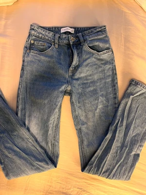 Blå high waist jeans från Pull&Bear - Säljer ett par klassiska blå jeans från Pull&Bear i storlek 34. Modellen är högmidjad med raka ben och femficksdesign. Jeansen har en snygg tvättad look och är tillverkade i slitstark denim med knapp och dragkedja framtill.