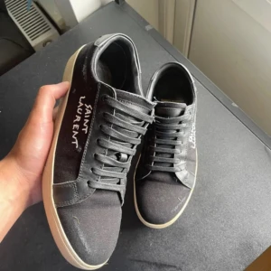 Svarta Saint Laurent sneakers - Svarta sneakers från Saint Laurent med vit logga broderad på sidan. perfekt nu inför hösten! finns box o dustbag.