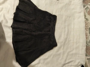 Svart kortkjol från FB Sister - Svart plisserad kortkjol från FB Sister i denim-look. Kjolen har bred resår i midjan och dragkedja med knapp i sidan. Snygg och enkel modell som ger en cool vibe till outfiten. Jättefin med tajts, några boots med en stickad tröja.