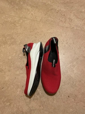 Röda slip-on sneakers med vit sula - Snygga röda slip-on sneakers med svart och vit tjock sula. Ovandelen är i mesh-liknande syntetmaterial och har en svart detalj med reflex vid hälen. Skorna har rund tå och är perfekta för dig som gillar sportig stil.