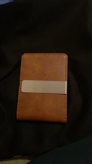 Brun plånbok med metallklämma - Slimmad brun plånbok i skinn med stilren metallklämma på utsidan. Insidan har flera kortfack och ett smart fack för sedlar. Perfekt för dig som vill ha en clean och praktisk look utan att ta upp för mycket plats i fickan.