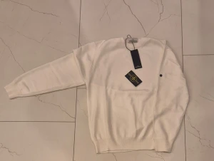 Vit tröja från Stone Island - Säljer en clean vit tröja från Stone Island med klassisk patch på vänster ärm. Tröjan har rund hals, ribbade muddar och en normal passform. Perfekt för dig som gillar stilrena plagg med ikoniska detaljer.
