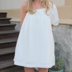 Vit kort omlottklänning med puffärm - Säljer min älskade studentklänning som har en inbyggd klänning för extra puff! Superfin vit kort klänning med en axel och puffärm. Perfekt till studenten eller skolavslutningen!